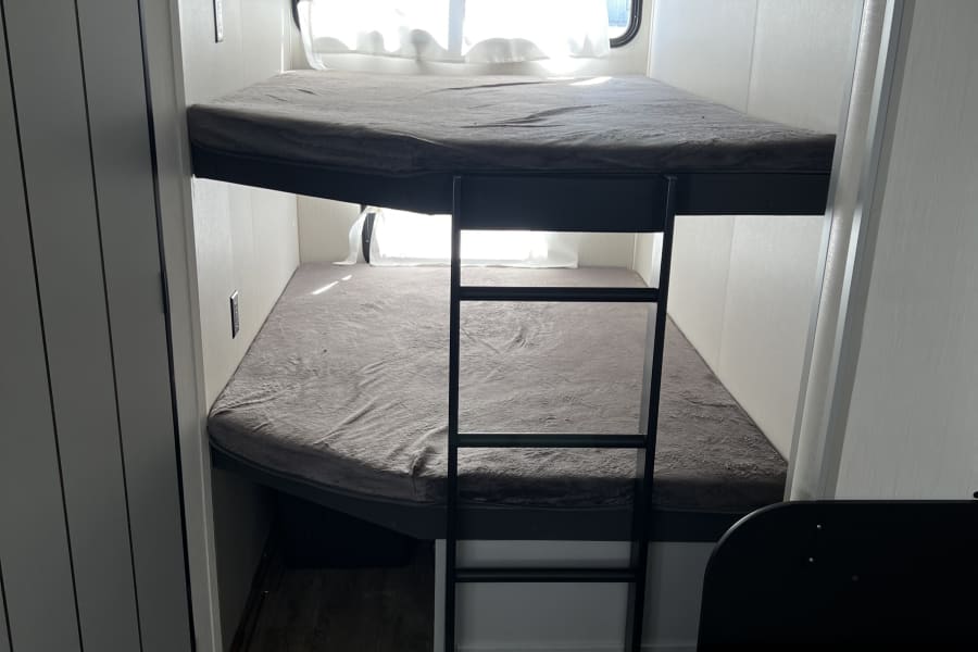 RV rental: Cozy interior featuring two bunk beds with grey mattresses, a black ladder, and bright windows.