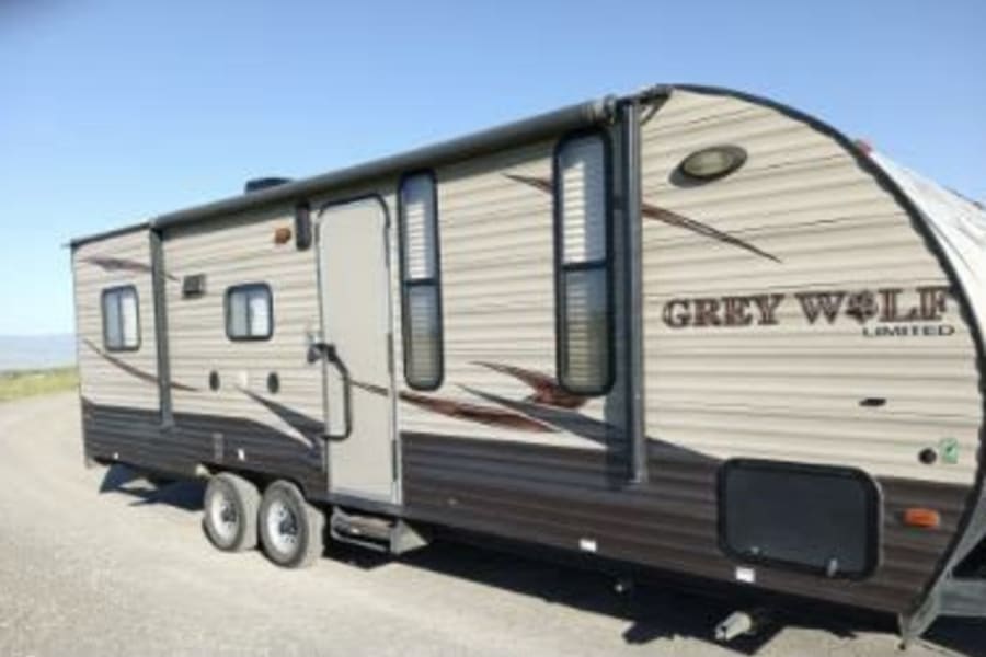 A beige and brown Grey Wolf travel trailer, perfect for RV rental, is seen parked.