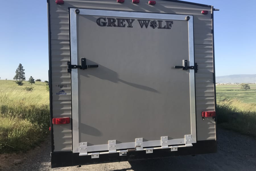 Rear view of a Grey Wolf travel trailer, ideal for an RV rental. Shows the large ramp door with latches, lights, and branding.