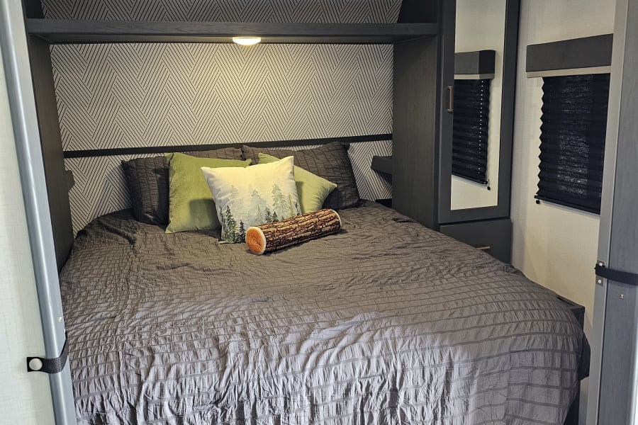Cozy RV rental bedroom featuring a comfortable bed, patterned wall, and integrated storage for a comfortable stay.