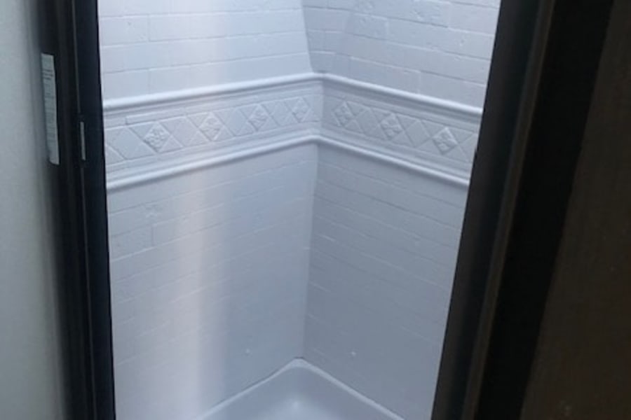 Clean white shower in an RV rental, with brick-look walls, decorative trim, a corner shelf, and shower pan.