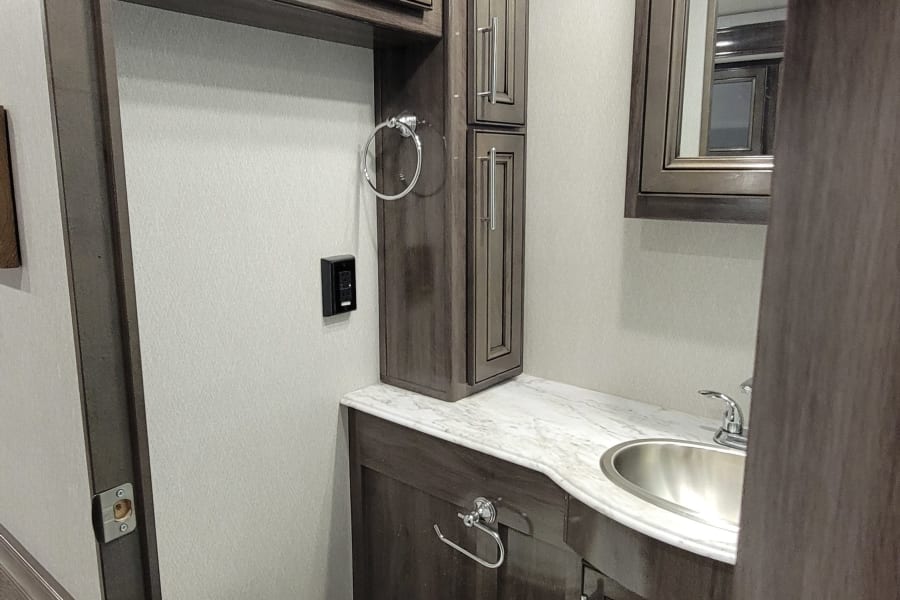 Modern compact RV rental bathroom with toilet, vanity sink, mirror, and dark wood storage cabinets.