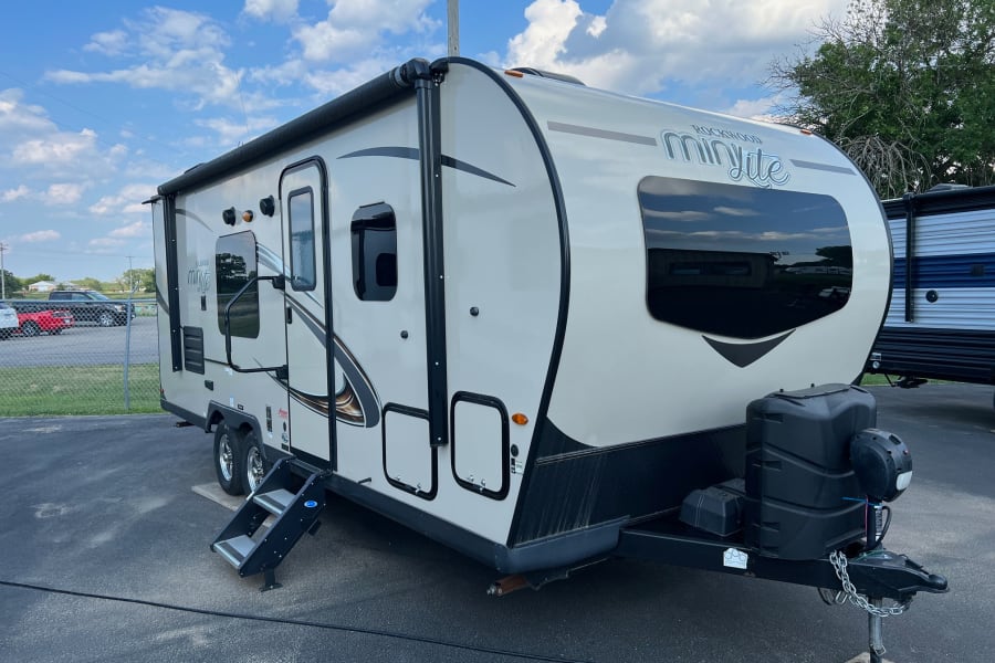 A modern beige Rockwood Mini Lite RV, perfect for your next rv rental adventure. Steps extended, ready for camping.