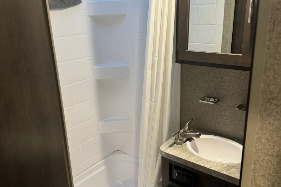 This compact RV rental bathroom features a shower-tub combo, vanity with sink, mirror, and efficient storage solutions.
