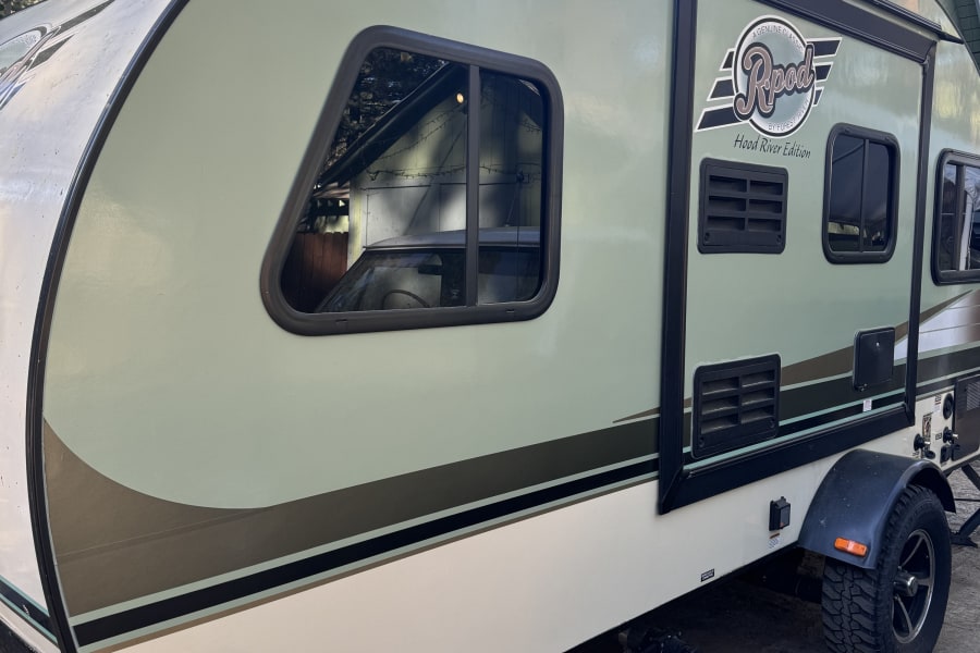 Side view of an R-Pod Hood River Edition RV rental, a light green travel trailer parked amidst trees. Perfect for getaways!