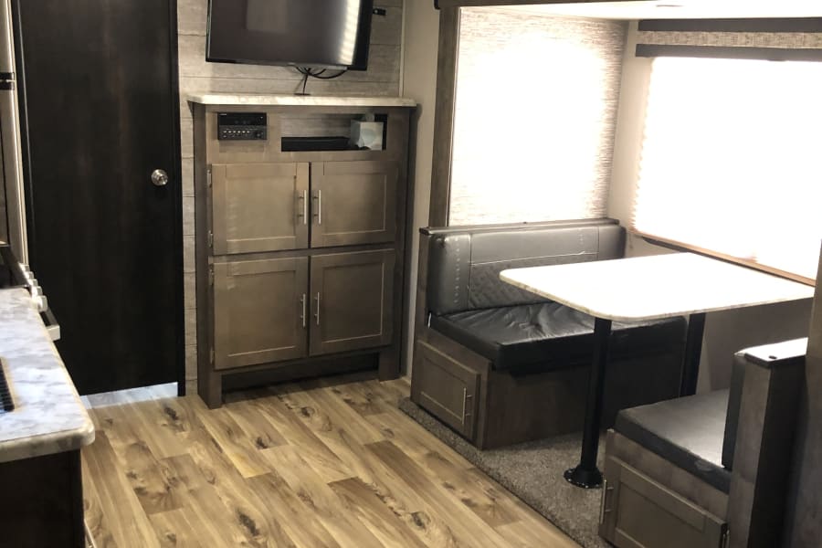 Cozy **rv rental** interior featuring a dinette, entertainment center, and wood-look flooring.
