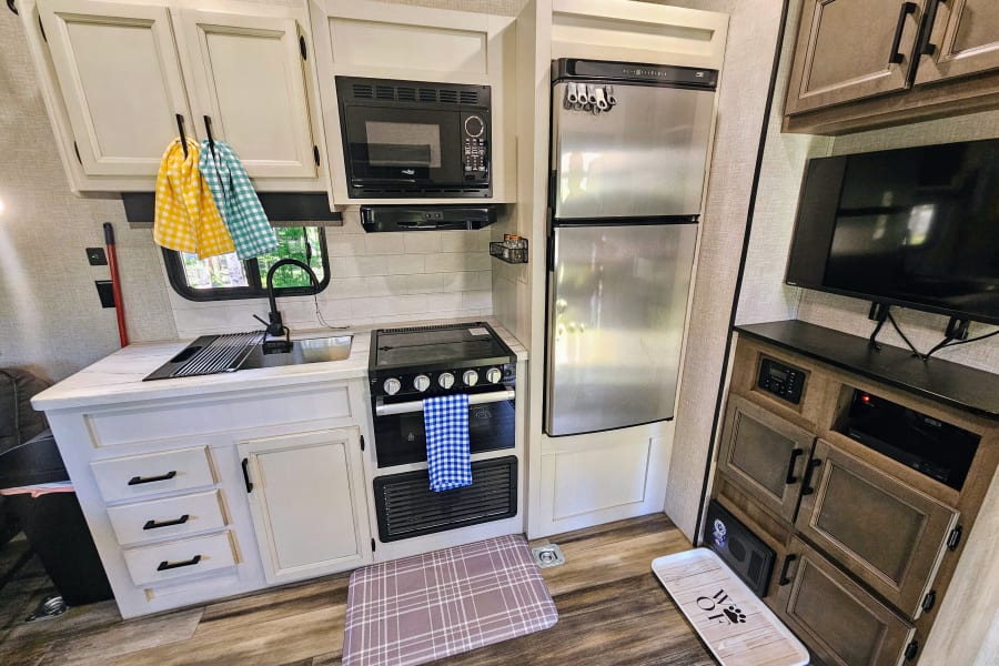 Spacious RV rental kitchen and living area with white cabinets, stainless steel fridge, and entertainment setup.