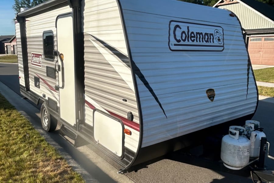Sleek white Coleman RV rental parked on a sunny street, ready for your next travel adventure or camping trip.
