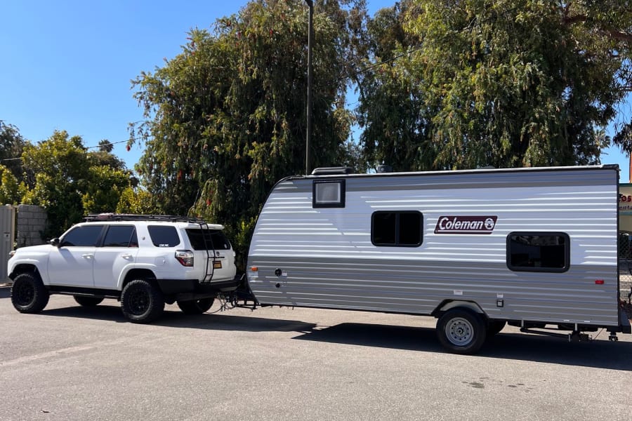 A white SUV towing a grey and white Coleman RV rental, ready for travel and outdoor adventures.