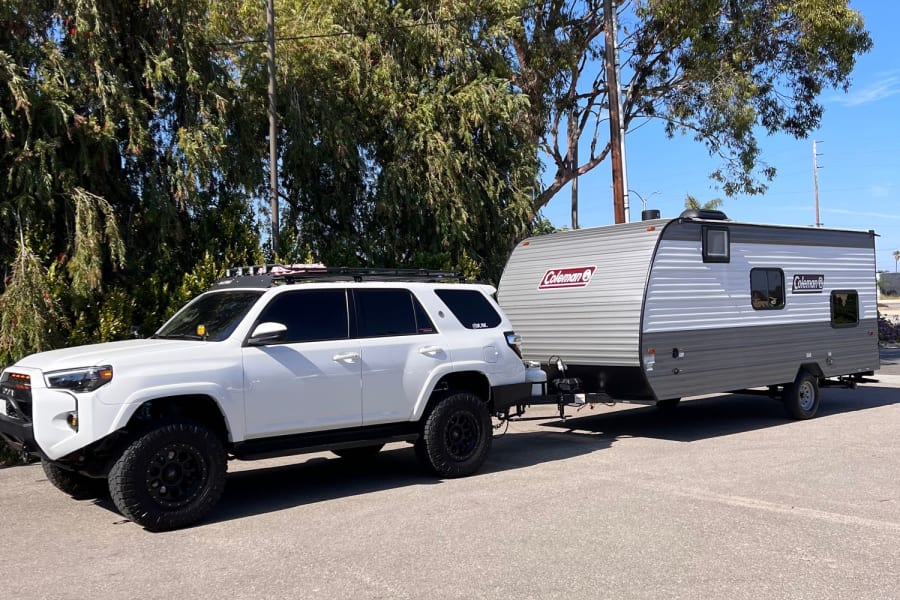 A white 4Runner SUV tows a grey Coleman travel trailer. Ideal setup for an rv rental or camping trip!
