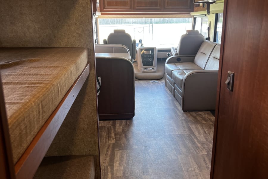 Spacious RV rental interior featuring comfortable bunk beds, a well-equipped driver's cockpit, and a cozy living area.