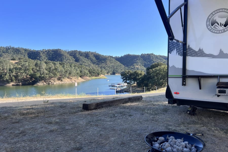 RV rental lakeside: Camper by a beautiful lake and hills with a fire pit, ideal for outdoor camping.