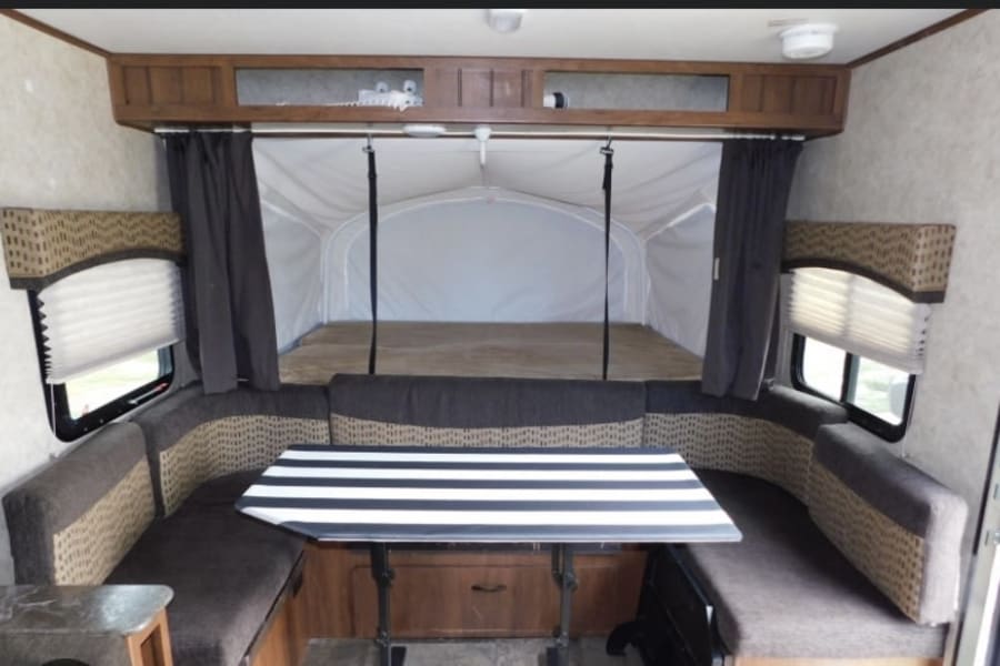 This RV rental interior features a cozy U-shaped dinette with a striped table, an expandable pop-out bed, and storage.