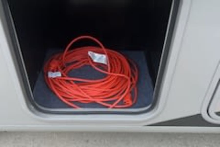 RV rental ready: A bright orange extension cord coiled in a clean, open storage bay of an RV.