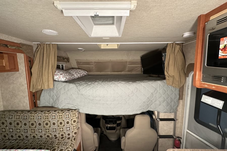 Cozy RV rental interior with bed, dinette, and cockpit view, perfect for road trips.