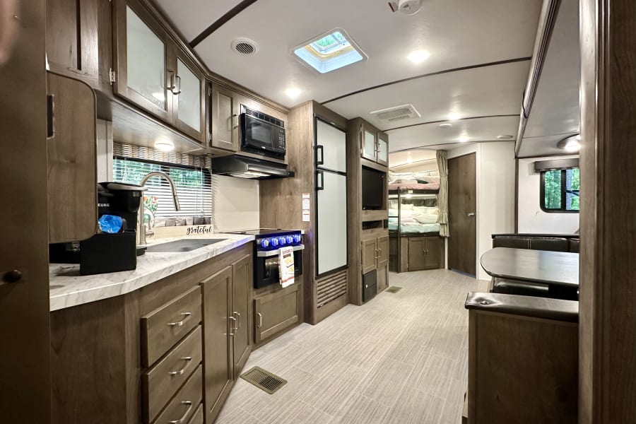 Spacious, modern RV rental interior featuring a full kitchen, dining area, and cozy bunk beds.
