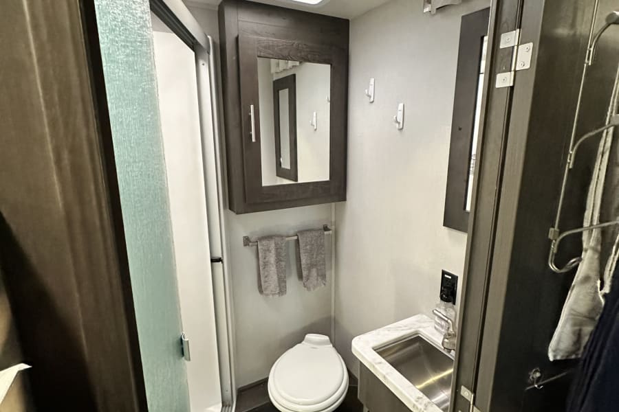 Compact and clean RV rental bathroom featuring a shower, toilet, sink, and medicine cabinet, optimized for travel comfort.