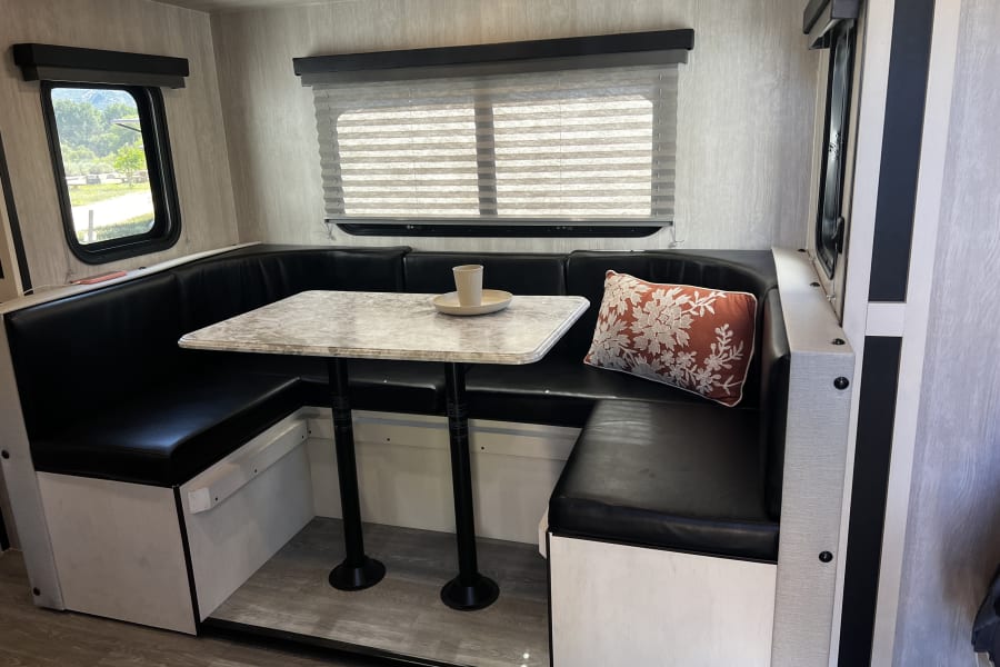 U-shaped dinette in an RV rental, featuring comfortable black seating, a marble-look table, and large windows.