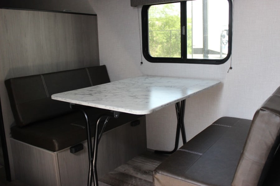 RV rental interior: This camper's dinette features a marble-patterned table and dark benches beside a window.
