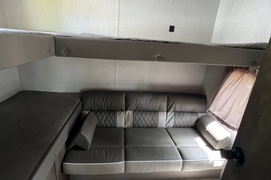 RV rental: Dark grey convertible sofa, upper bunk, and lower bunk/bench. Light walls, herringbone floor.