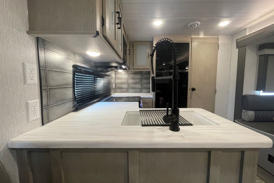 RV rental kitchen: stylish interior with white countertops, sink, black faucet, light wood cabinets, and cozy seating.