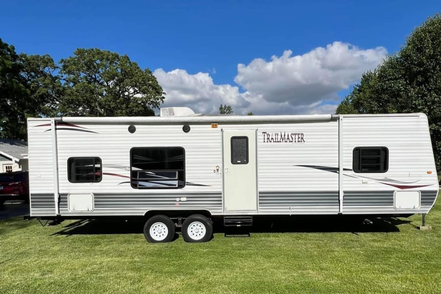 White TRAILMASTER travel trailer, ideal for rv rental adventures. This large camper is parked on green grass.