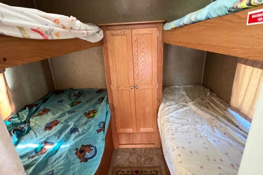 RV rental bunk beds. Cozy sleeping area in a camper with two sets of bunks, fun bedding & central cabinet. Max 125 lbs.