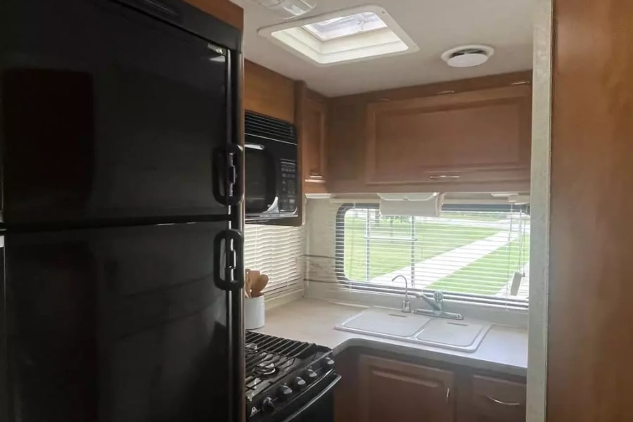 Spacious RV rental kitchen featuring a large black refrigerator, microwave, stove, and double sink with a window view.