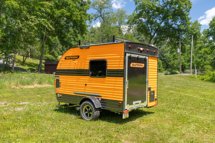 Orange SUNRAY Sport teardrop RV rental parked in grass, ready for adventure.