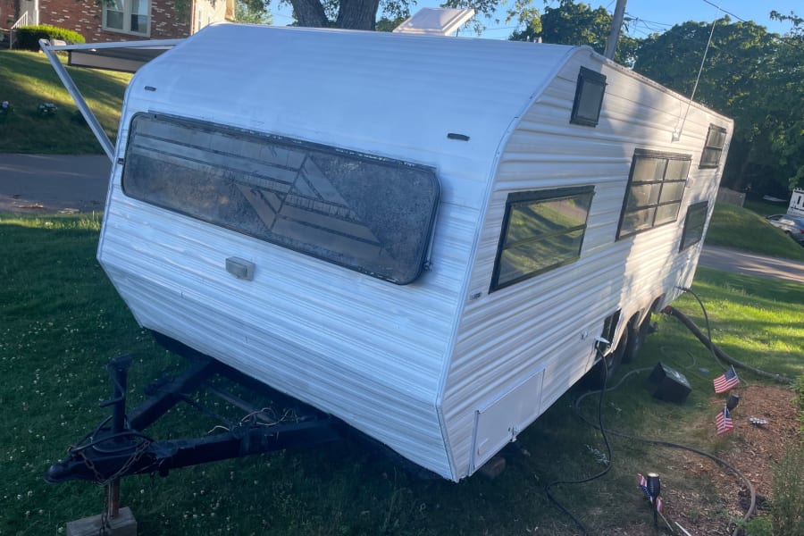 White travel trailer with an extended awning, parked on grass. Great for your next RV rental adventure.
