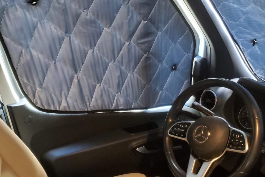 RV rental: Cozy Mercedes-Benz van interior featuring quilted window insulation and comfy beige seats.