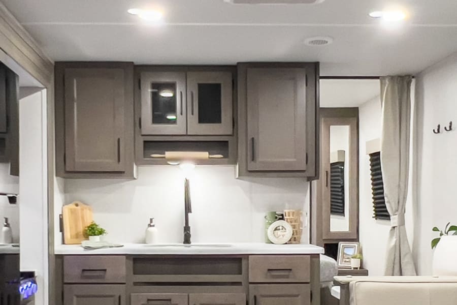 Modern RV rental interior: a sleek kitchen with brown cabinets, white counters, and wood-look flooring.
