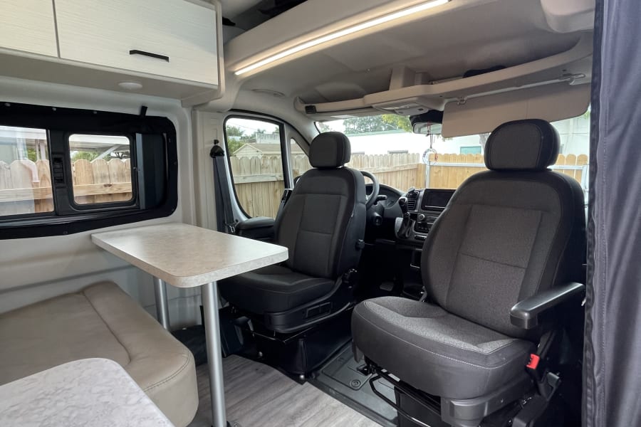 Bright RV rental interior with swivel front seats, dining table, and ample storage, perfect for your camper van adventure.