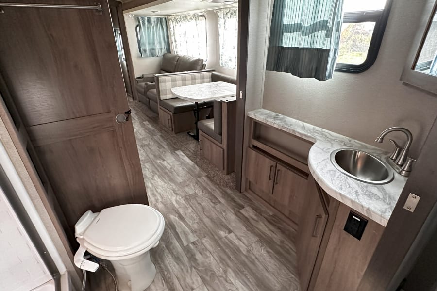 Spacious RV rental interior with a functional bathroom, including toilet and sink, plus a dinette and sofa. Ready for adventure!