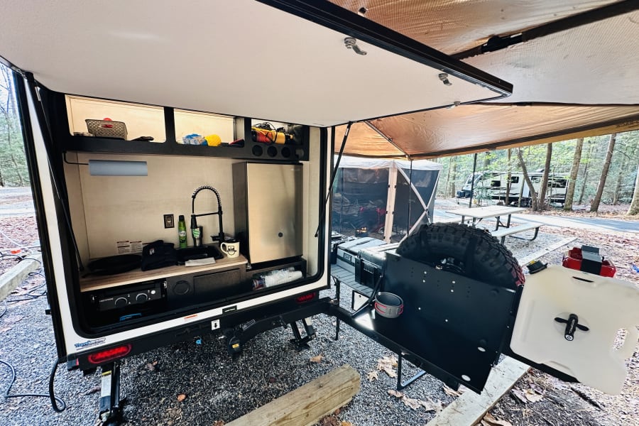 Camping with this compact RV rental! Enjoy the outdoor kitchen, sink, fridge, and shaded awning at your campsite.