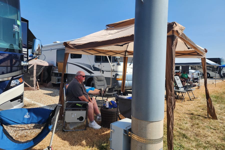 Sunny day at an RV rental camp: people relax under a canopy near their motorhomes.