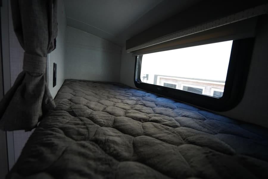 Cozy bunk bed in an rv rental, featuring a plush gray comforter and a bright window with a view outside.