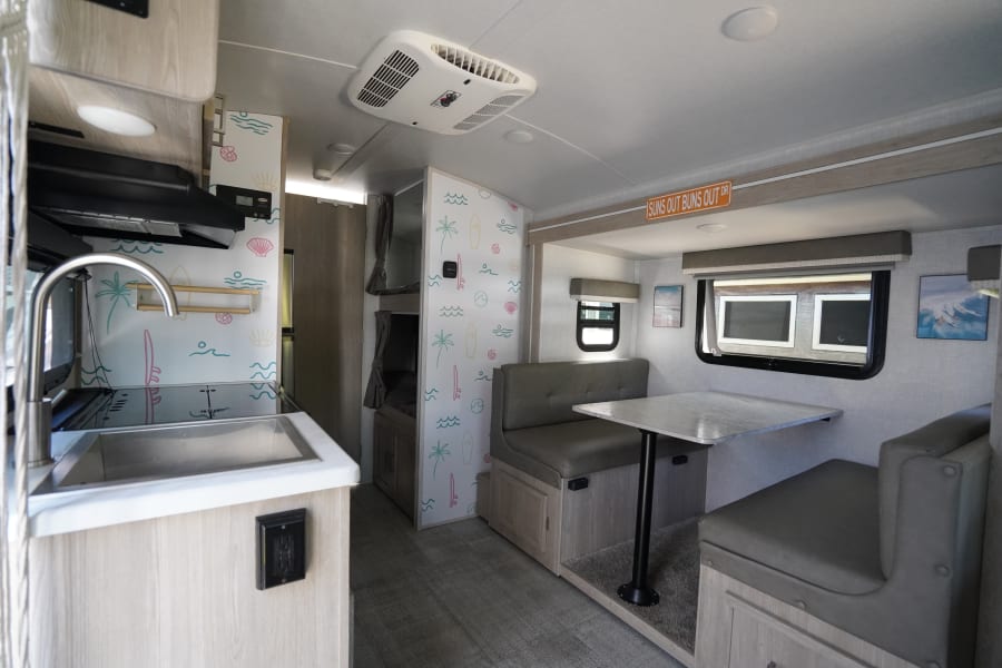 Bright, beach-themed RV rental interior showing a kitchen, dinette, and bunk beds, ideal for a travel trailer adventure.