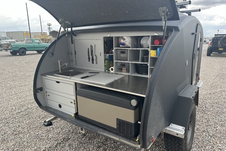Compact RV rental: Teardrop trailer's organized outdoor kitchen with sink, fridge, and storage, perfect for camping adventures.