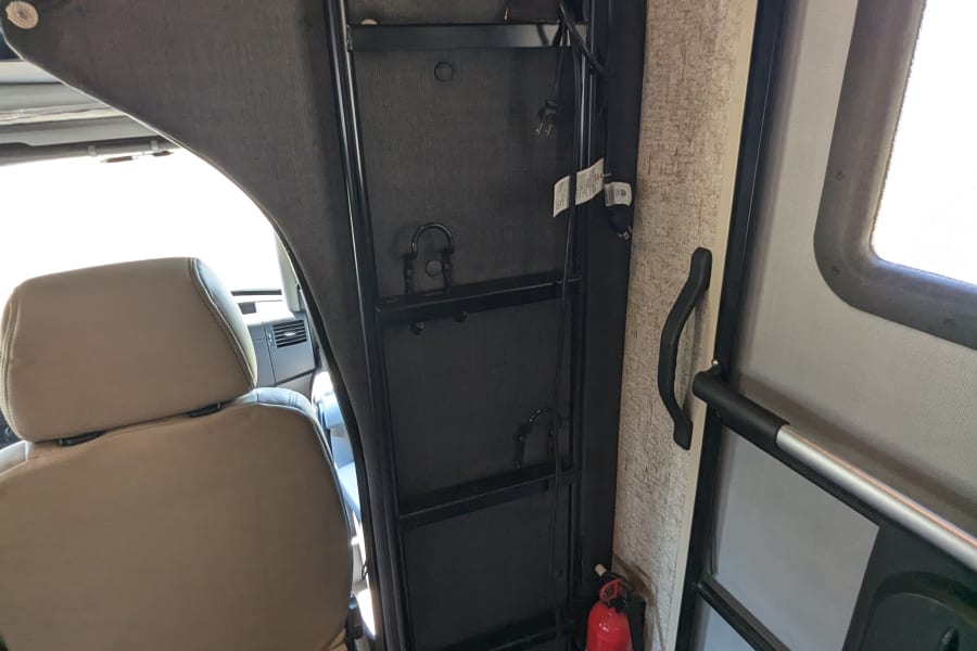 RV rental interior featuring a bunk bed with ladder, driver's seat, a fire extinguisher, and the entry door.