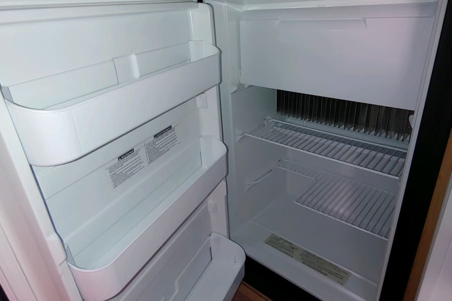 Open, empty RV rental fridge showing its compact interior shelves and door storage, ideal for travel.