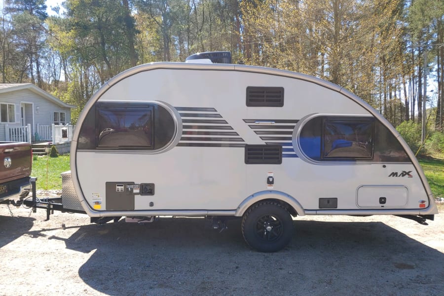 This sleek, silver teardrop travel trailer is an ideal rv rental for outdoor adventures, parked on gravel and hitched to a truck.