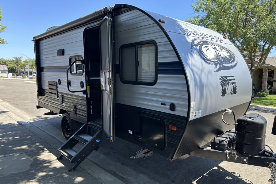 This RV rental travel trailer, gray and black with steps and rolled awning, is ready for adventure.
