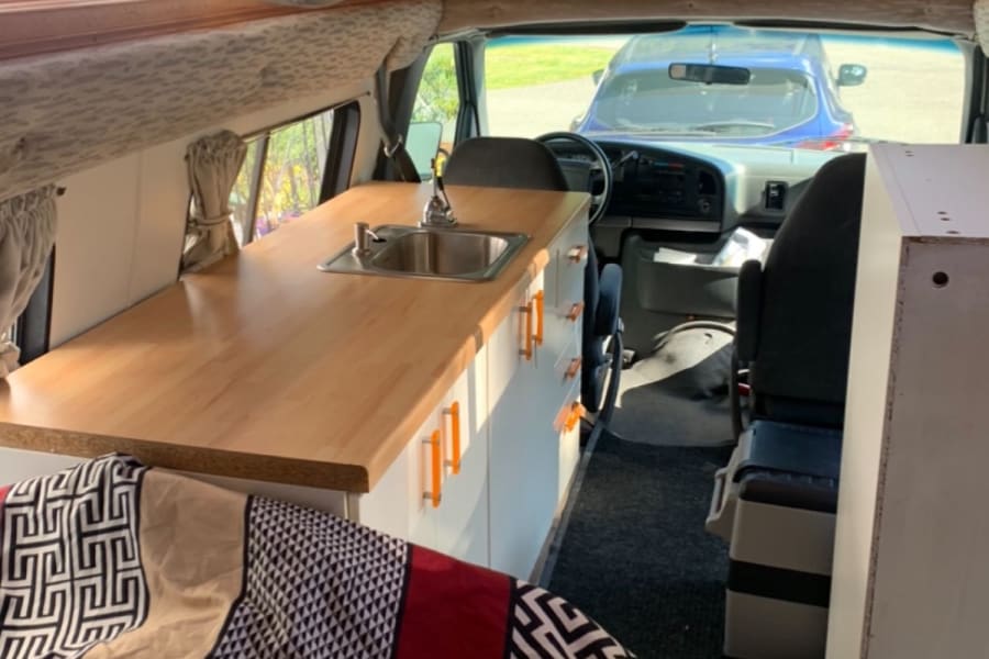 Cozy RV rental interior with wooden ceiling, full kitchenette, and bedding, ideal for mobile living and van life adventures.