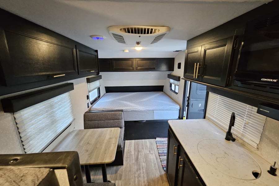 Inside this RV rental: a modern interior with a comfortable bed, dinette, and kitchenette. Ready for your next travel adventure!
