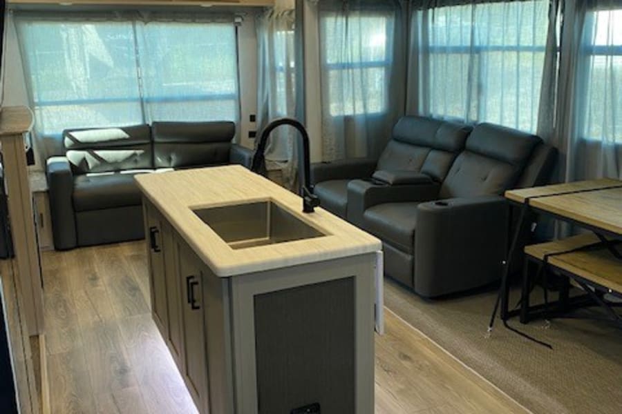 Spacious modern RV rental interior with illuminated kitchen island, wood flooring, cozy seating, & ambient lighting.