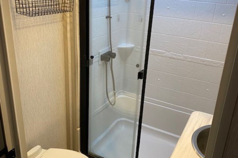 Compact RV rental bathroom featuring a toilet, glass-enclosed shower, small sink, and wall storage baskets.