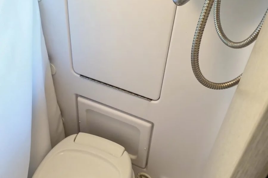 An RV rental's compact wet bath showing a white toilet, shower head, and curtain for a small, functional space.