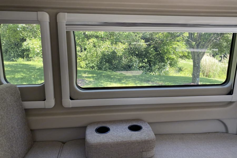 This RV rental features a comfortable lounge area with cup holders and serene nature views from its large windows.