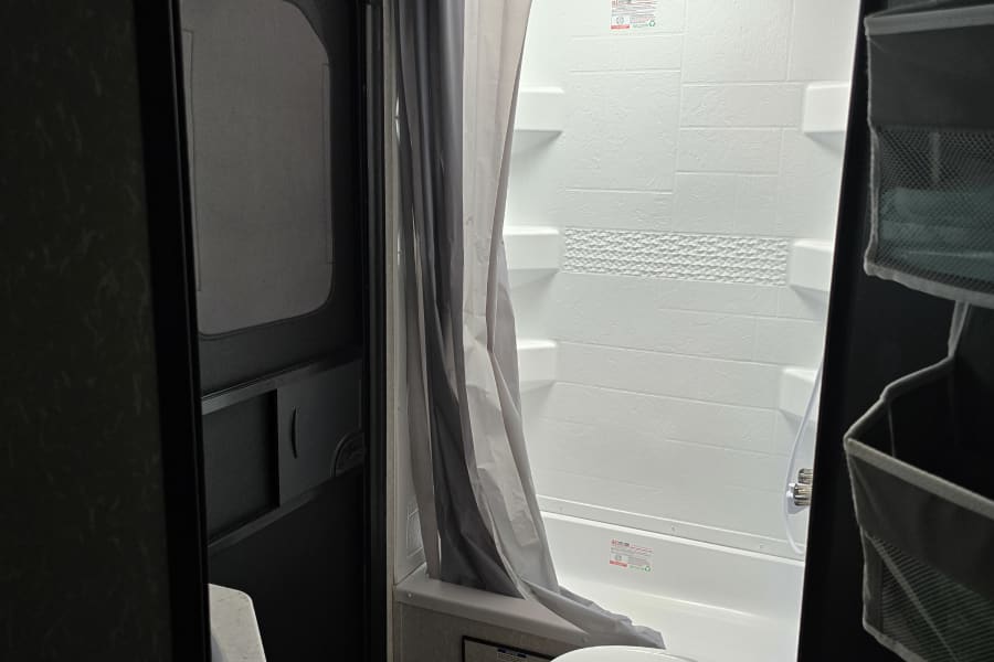 RV rental bathroom interior: Compact shower, toilet, and sink visible through the open door, ready for travel.
